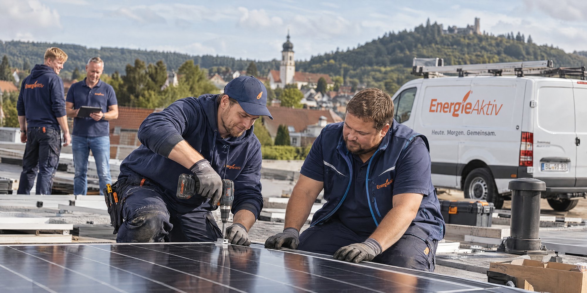 Monteure von EnergieAktiv montieren eine Photovoltaikanlage auf einem Dach, im Hintergrund Kirchturm und Burg der Region