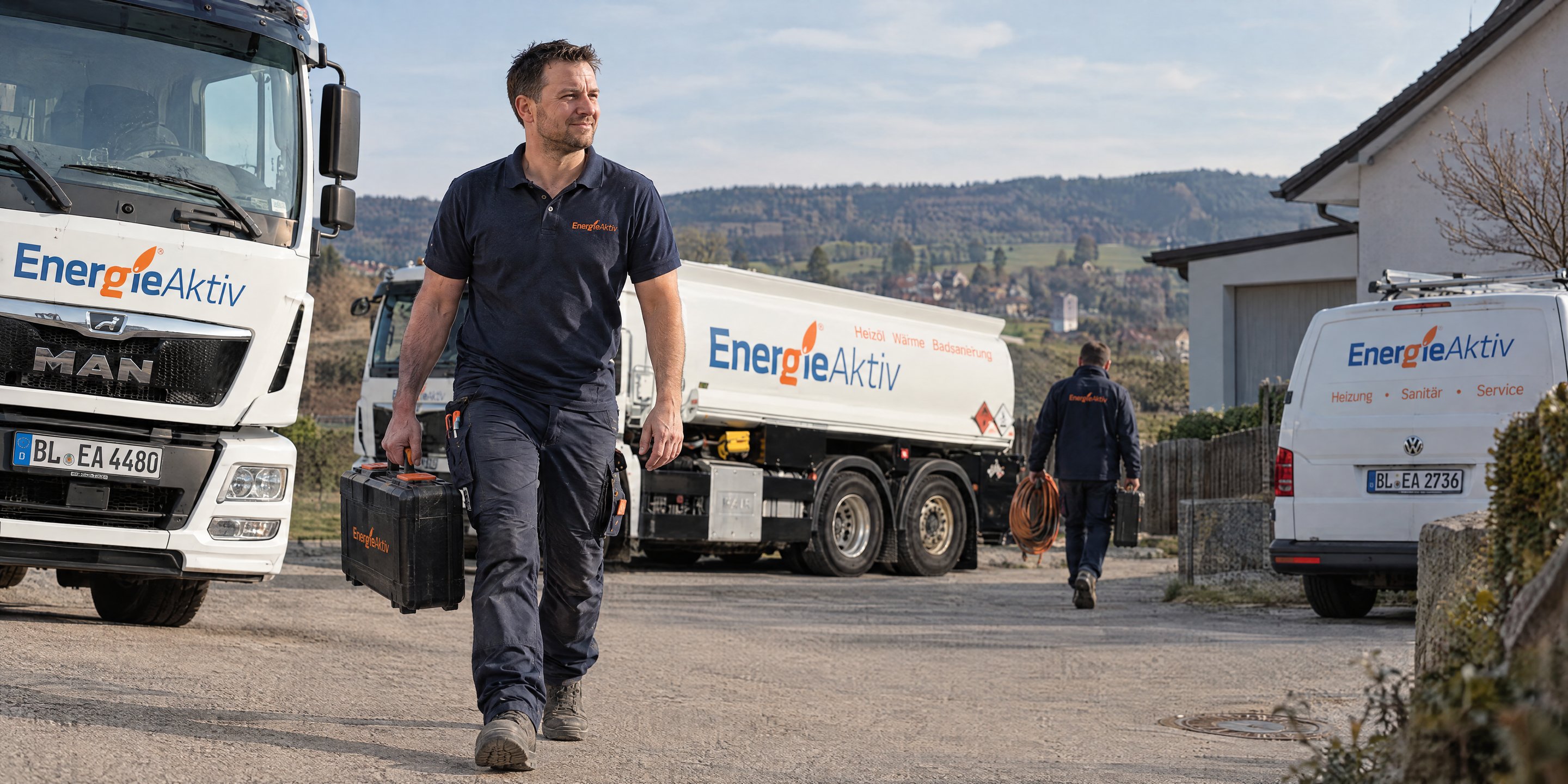 Monteur von EnergieAktiv mit Werkzeugkoffer vor Tankwagen und Servicewagen auf dem Weg zum Kunden